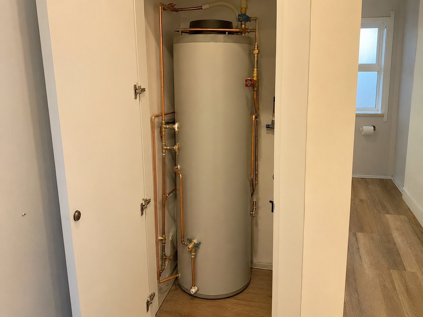 New hot water cylinder with tidy copper pipework in a hallway cupboard
